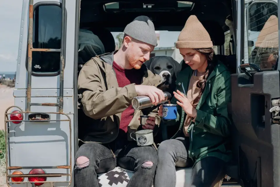 A dog drinking water from a collapsible travel bowl next to an open car door