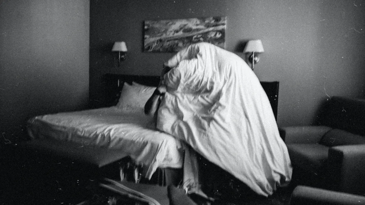 A dog lying calmly on a folded blanket beside an open suitcase in a hotel room