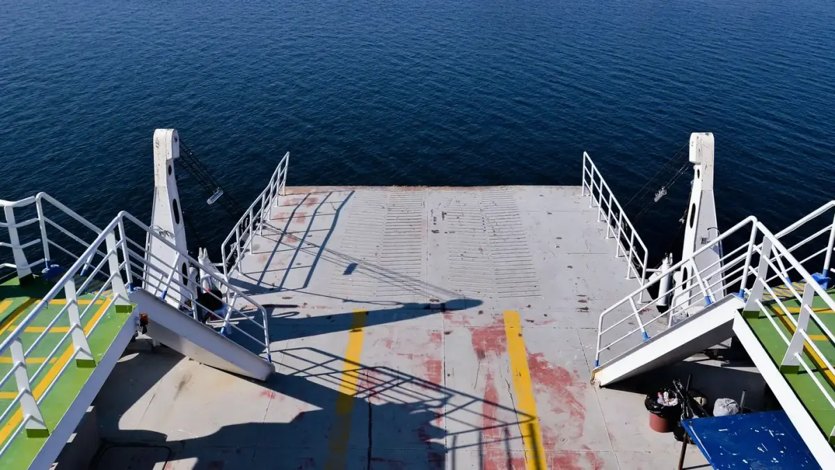 A leashed dog standing at the railing of a ferry deck with open water behind it