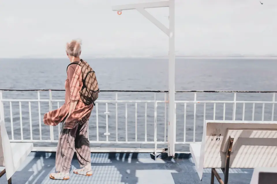 A leashed dog standing at the railing of a ferry deck with open water behind it