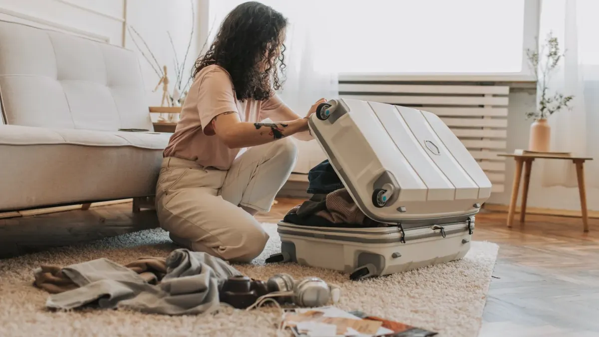 A woman reviewing travel paperwork at a table with her dog resting beside a packed suitcase